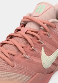 Gros plan d'une chaussure de sport rose avec des lacets détaillés, un tissu texturé, un swoosh Nike blanc et un logo vert sur la languette.