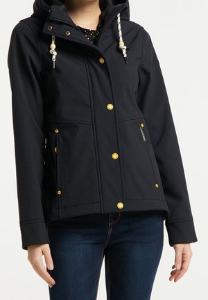 Schwarze Kapuzenjacke mit goldenen Druckknöpfen, weißen Kordeln mit Holzperlen, getragen über dunkelblauen Jeans.