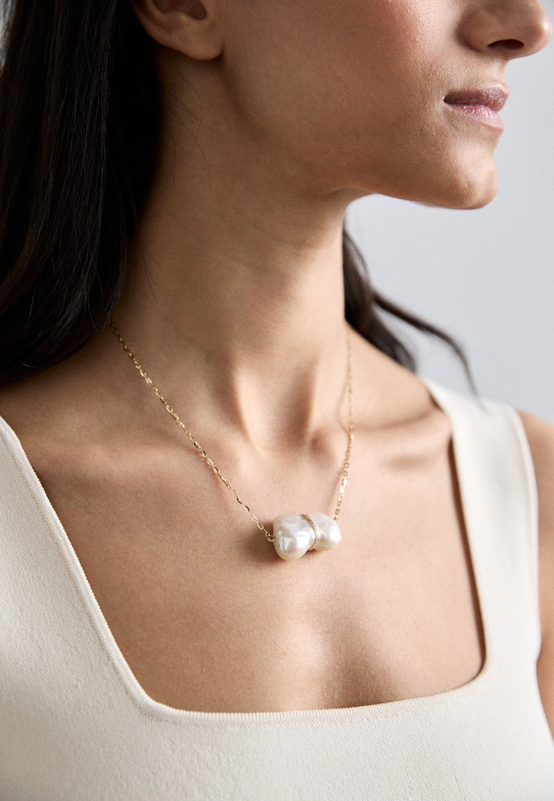 Guldkæde med en asymmetrisk hvid perle, der viser en glat tekstur og en unik organisk form.
