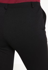 Svarta åtsittande byxor gjorda av ett slätt tyg med en stilren design. Har en midja och sidofickor för funktionalitet.