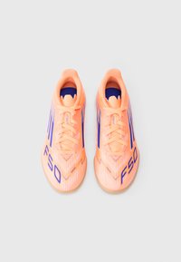 Un paio di scarpe da calcio indoor di un luminoso arancione con branding e lacci blu "F50", viste dall'alto su uno sfondo bianco.