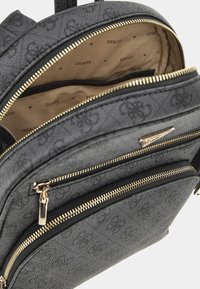 Schwarzer, strukturierten Rucksack mit goldfarbenen Reißverschlüssen, mehreren Taschen und einem marken-logo-muster in hellbraunem Innenfutter.