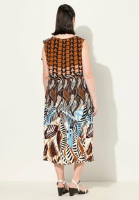Robe multicolore avec un haut à motifs de formes géométriques, une jupe à motif de feuilles et un col uni. Portée avec des sandales à talons hauts.