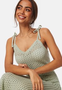 Abito lavorato a maglia verde chiaro con scollatura a V, motivo traforato e spalline regolabili. Texture liscia e vestibilità comoda.