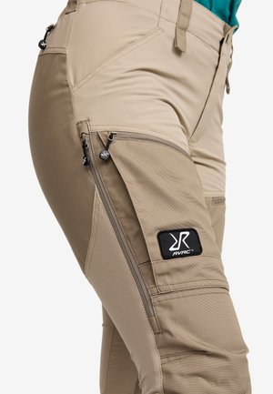 Beige Outdoor-Hosen mit mehreren Reißverschlusstaschen, verstärkten Nähten und einem schwarzen RVRC-Logo-Patch am Oberschenkel. Glattes, strapazierfähiges Material.