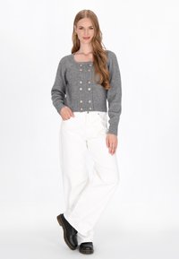 Grå ribbad kort cardigan med fyrkantig halsringning och guldknappar, i kombination med vita vida byxor och svarta skor.
