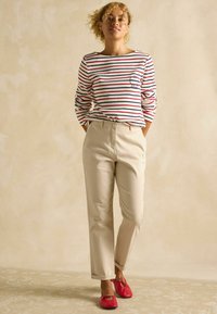 Svītrains, garām piedurknēm krekls baltā, sarkanā un tumši zilā krāsā; bēšas krāsas chino bikses; sarkani dzīvokļu apavi ar lokām; brīvs piegriezums; vienkāršs fons.