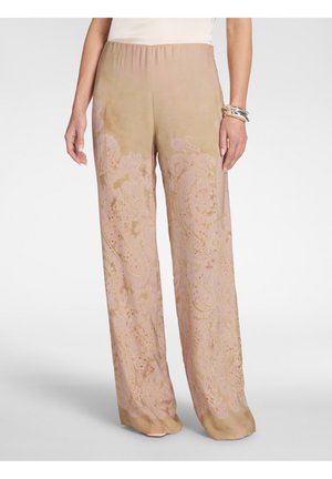 Pantalon beige ample avec des motifs paisley roses subtils, taille élastique, porté avec un haut blanc et des bracelets argentés au poignet droit.
