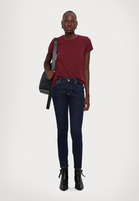 Burgundy short-sleeve t-shirt paired with dark blue skinny jeans. Model wears black ankle boots and carries a black shoulder bag.