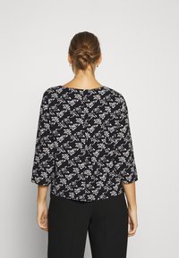 Svartvitt mönstrad blus med trekvartslånga ärmar, rund hals, och en avslappnad passform, med en något böjd nederkant och detaljer i sömmen på ryggen.