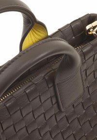 Geweven leren handtas in donkerbruin met gele interieuraccenten. Voorzien van een ritssluiting en ronde handvatten. Gelaagde oppervlaktelijst.