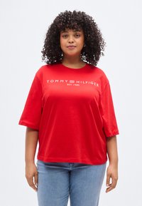 Κόκκινο βαμβακερό T-shirt με κοντά μανίκια, με λευκό λογότυπο «TOMMY HILFIGER EST. 1985» στο μπροστινό μέρος. Χαλαρή εφαρμογή, λεία υφή.