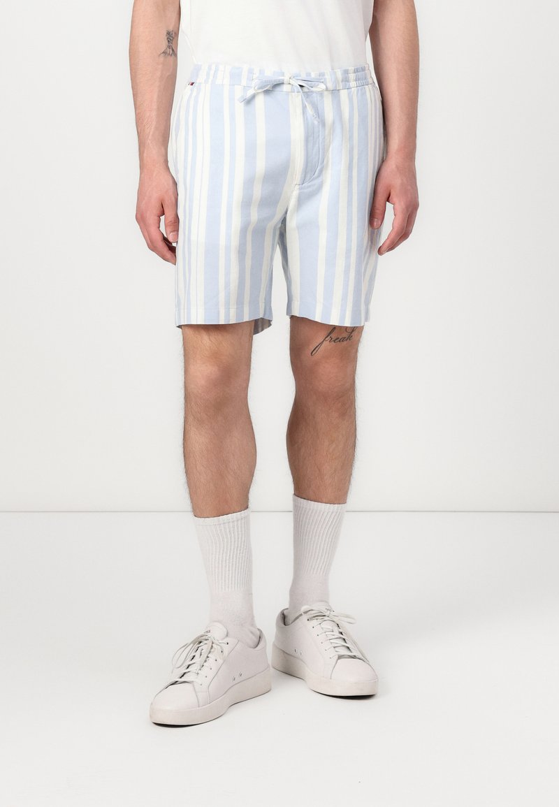 Shorts de bain rayés bleus clairs et blancs, fabriqués dans un tissu doux, avec une taille élastique et un cordon de serrage.