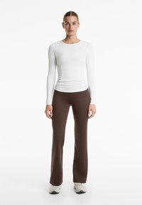 Top alb cu mâneci lungi, ajustat, și pantaloni maroon evazați, confecționați dintr-un material elastic. Ținuta este accessorized cu adidași de culoare deschisă.