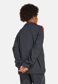 Donkerblauwe jas van lichtgewicht materiaal, met rode schouderstrepen en elastische boorden. Eenvoudig ontwerp met een relaxte pasvorm.