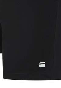 Schwarze sportliche Shorts aus weichem Material. Mit einem weißen Logo am unteren Bein. Minimalistisches Design mit klaren Linien und ohne sichtbare Muster.