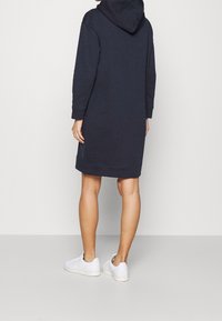 Vestito con cappuccio blu navy in tessuto morbido, caratterizzato da maniche lunghe, tasca a marsupio e polsini a coste, abbinato a sneakers bianche.