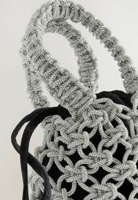 Juodas audinių maišelis su sidabrinėmis karoliukų rankenomis. Rankenos turi susuktą raštą, sukurdamos tekstūruotus akcentus prieš lygiu maišelio paviršiumi.