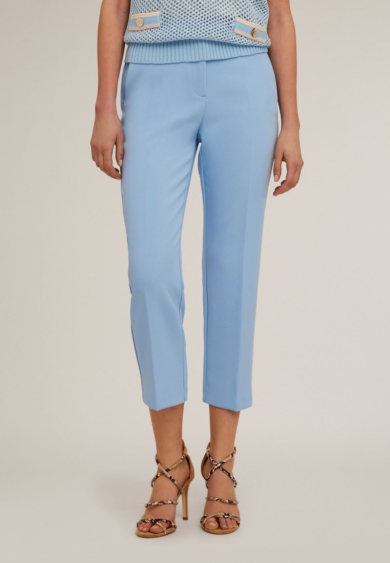 Pantalons cropped bleu clair en tissu lisse, avec une coupe slim et une taille plate. Associés à des chaussures à talons hauts avec lanières.