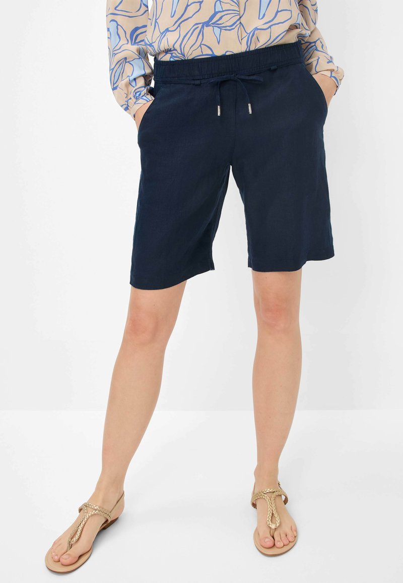 Mørkeblå linnedshorts med elastisk talje, snoretræk og sidelommer, kombineret med beige sandaler.