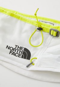Borsone in rete bianco con accenti giallo neon, presenta un cordino e una fibbia regolabili, logo stampato in nero. Superficie testurizzata e design leggero.
