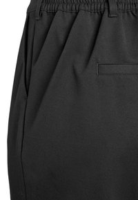 Melnas bikses ar elastīgu vidukļa joslu, mīkstu audumu, krokotu dizainu un vienu aizmugurējo kabatas detaļu. Gluda tekstūra un piegriezts siluets.