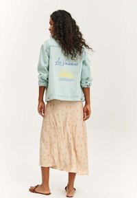 Svetlomodrá džínsová bunda s výšivkou "Les Vacances" a dizajnom slnka na chrbte, v kombinácii s béžovou sukňou s kvetinovým vzorom.