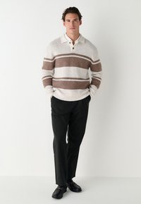 Krémový a hnedý pruhovaný pletený sveter s golierom, kombinovaný s tmavými nohavicami a čiernymi topánkami. Mäkká textúra a pohodlný strih.