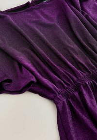 Robe en tissu violet scintillant avec taille élastiquée froncée et manches courtes, posée à plat sur une surface claire.