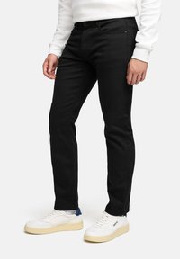 Jeans neri skinny, realizzati in denim, con un classico design a cinque tasche. Indossati con sneakers bianche e una felpa bianca.