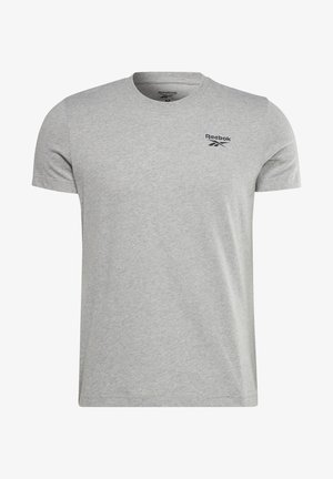 Mann trägt graues Reebok-T-Shirt, marineblaue Jogginghose, weiße Turnschuhe und hält eine große blau-schwarze Sporttasche an den Griffen.