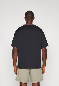 Černé tričko s krátkým rukávem a volným střihem, vyrobené z bavlny, s malým logem Nike na zadní straně, v kombinaci se šedými šortkami.