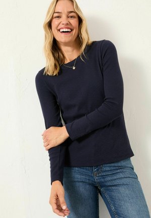 Marineblaues Langarmoberteil aus strukturiertem Stoff mit Rundhalsausschnitt und lockerer Passform, kombiniert mit Jeans.