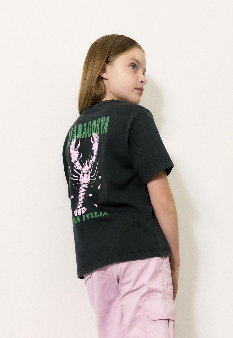 Czarny bawełniany t-shirt z różowym grafikiem homara i zielonym napisem na plecach. Krótkie rękawy, luźny krój i miękka tekstura.