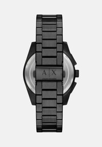 Črno nerjavno jeklo zapestnica s povezavami, osemkotna ohišje in vgraviran logotip na sponki. Ima minimalističen dizajn in gladko teksturo.