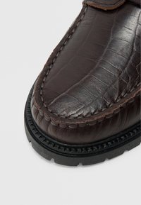 Σκούρο καφέ δερμάτινο μοκασίνι με υφή που μοιάζει με κροκόδειλο, λεπτομερή ραφή και αντιθετική σόλα από καουτσούκ.