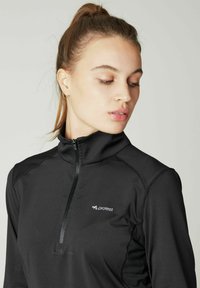 Schwarzes, zip-freies Sportoberteil mit hohem Kragen, aus strukturiertem Stoff und dezentem Logo auf der linken Brust. Glattes, enges Design.