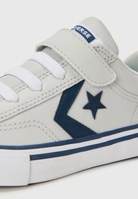 Graue Sneaker mit weißen Schnürsenkeln und Klettverschluss. Merkmale ein blaues Stern- und Zickzackmuster an der Seite, Gummisohle und gestickte Details.