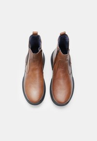 Botas de tobillo de cuero marrón con cremalleras laterales, con una textura suave y suelas de goma negra. El interior tiene un forro azul.