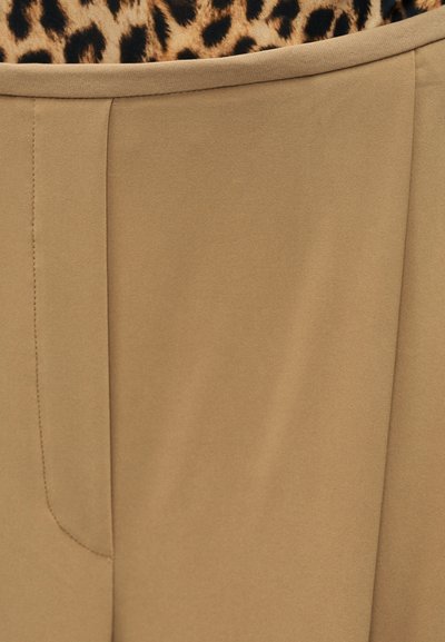 Μπεζ ύφασμα με λείο υφή, διαθέτει δομημένη μέση και διακριτικές λεπτομέρειες ραφής. Λεοπάρ σχέδιο ορατό πάνω από την τζιν περιοχή.