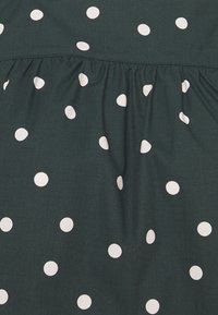 Tissu vert foncé à pois blancs, avec une texture froncée le long de la couture, créant un effet doux et drapé.