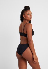 Μαύρο μπικίνι με απλό σχέδιο; ρυθμιζόμενες τιράντες, ψηλόμεσα σλιπ, λεία υφή και ελάχιστες λεπτομέρειες.