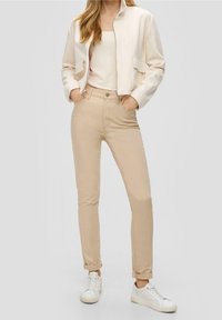 Chaqueta cremallera crema, pantalones beige ajustados y zapatillas blancas. Textura suave, diseño sencillo con dos bolsillos frontales y puños doblados en los pantalones.