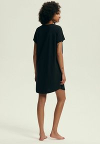 Czarna bawełniana sukienka typu T-shirt z krótkimi rękawami, luźnym krojem i zaokrąglonym dołem, prezentująca gładką teksturę i minimalistyczny design.