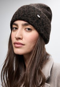 Gorro de punto marrón con un patrón texturizado y borde vuelto, que presenta un pequeño pin de logo plateado en el lateral.