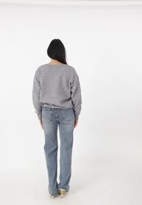 Maglione grigio a maniche lunghe, con piccoli motivi a cuore dorato sulle maniche. Abbinato a jeans di denim azzurro chiaro.