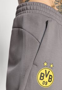 Grå atletiske shorts med elastisk talje, med et gult rundt logo med "BVB 09" og to stjerner. Materialet ser blødt og tekstureret ud.