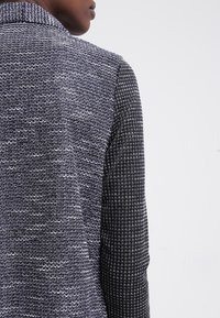 Stickad jacka med ett strukturerat blått och vitt mönster på ena sidan och en svart geometrisk design på den andra, med en formad krage.