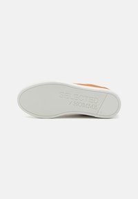 Fehér sneaker talp, amely texturált tapadással rendelkezik, és egy diszkrét, „SELECTED/HOMME” logó látható rajta. A felsőrész barna velúr kiegészítéssel rendelkezik.