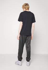 Černé bavlněné tričko s krátkými rukávy, doplněné tmavě šedými saténovými tepláky a šedými teniskami. Oblečení působí uvolněně a neformálně.